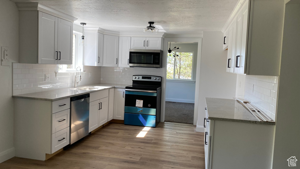 Kitchen featuring tasteful backsplash, white cabinetry, light hardwood / wood-style flooring, sink, and stainless steel appliances