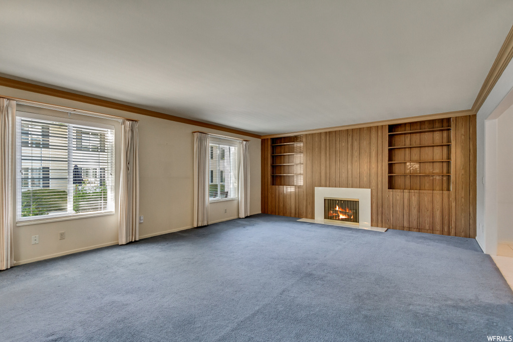 Carpeted living room featuring a fireplace, wooden walls, crown molding, and built in shelves