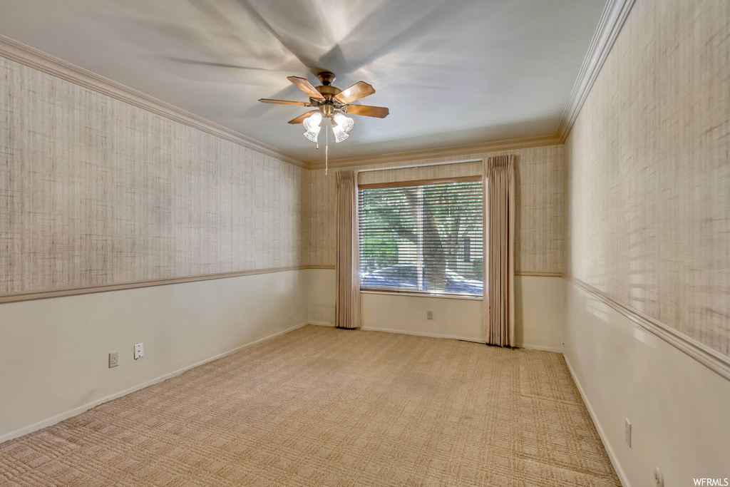 Empty room featuring ornamental molding, light carpet, and ceiling fan