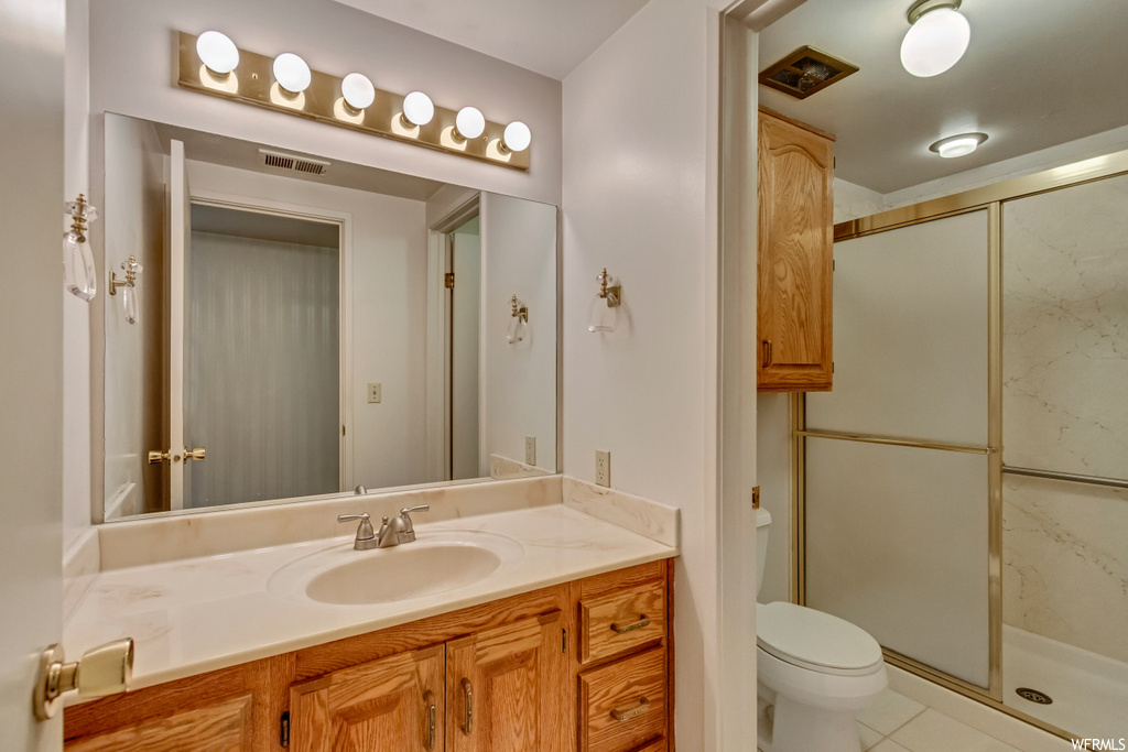 Bathroom featuring large vanity, light tile floors, mirror, and a shower with door