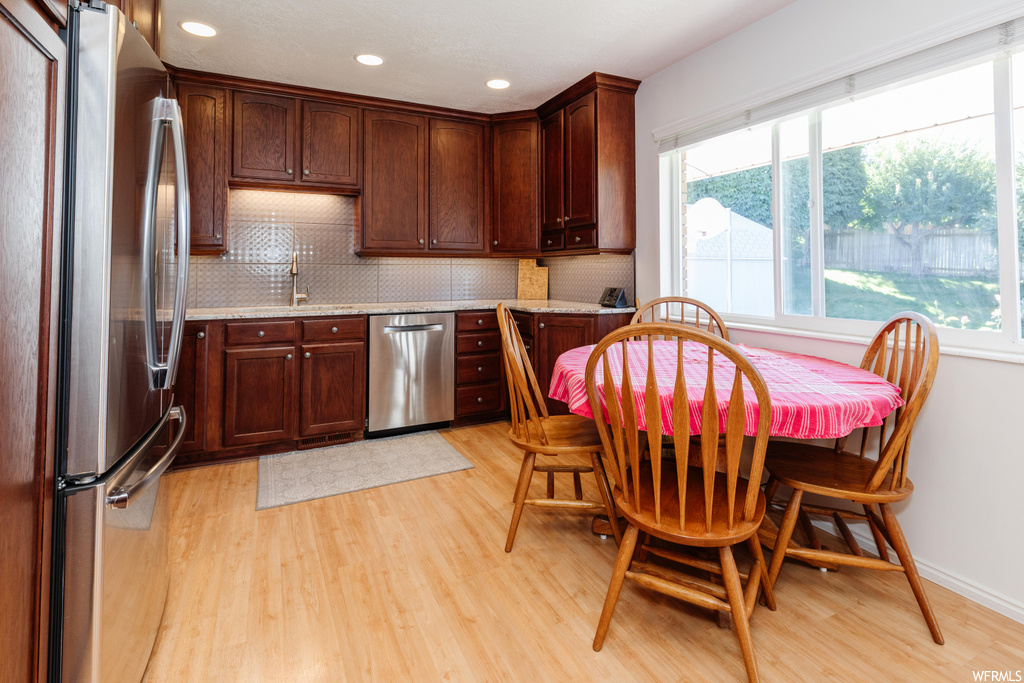 Kitchen featuring backsplash, light countertops, light hardwood floors, dark brown cabinetry, and stainless steel appliances