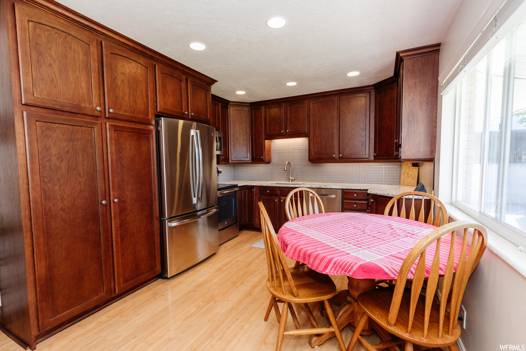 Kitchen with dark brown cabinets, light hardwood floors, backsplash, and stainless steel appliances