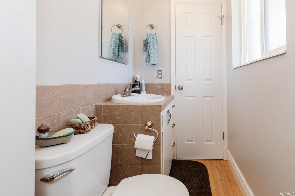Bathroom featuring mirror, tile walls, sink, and light hardwood flooring