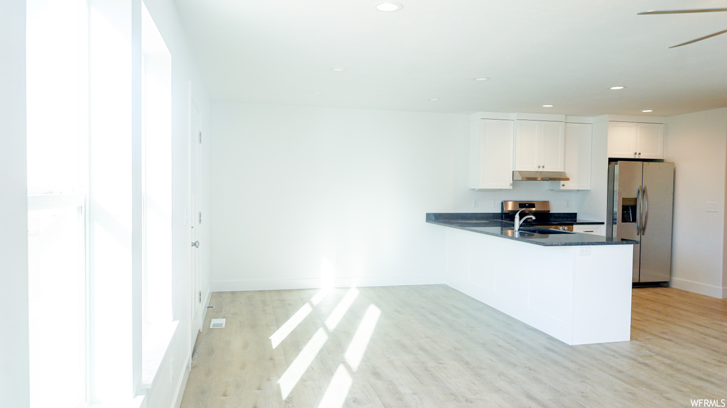 Kitchen with kitchen peninsula, stainless steel fridge, white cabinets, and light hardwood flooring