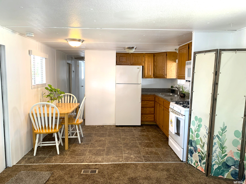 Kitchen featuring white appliances, countertops dark, dark colored carpet, and washbasin