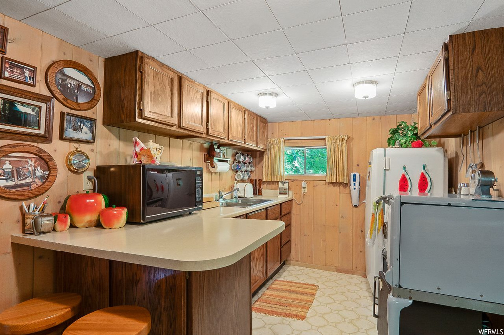 Kitchen featuring light tile floors, sink, wood walls, kitchen peninsula, and countertops light