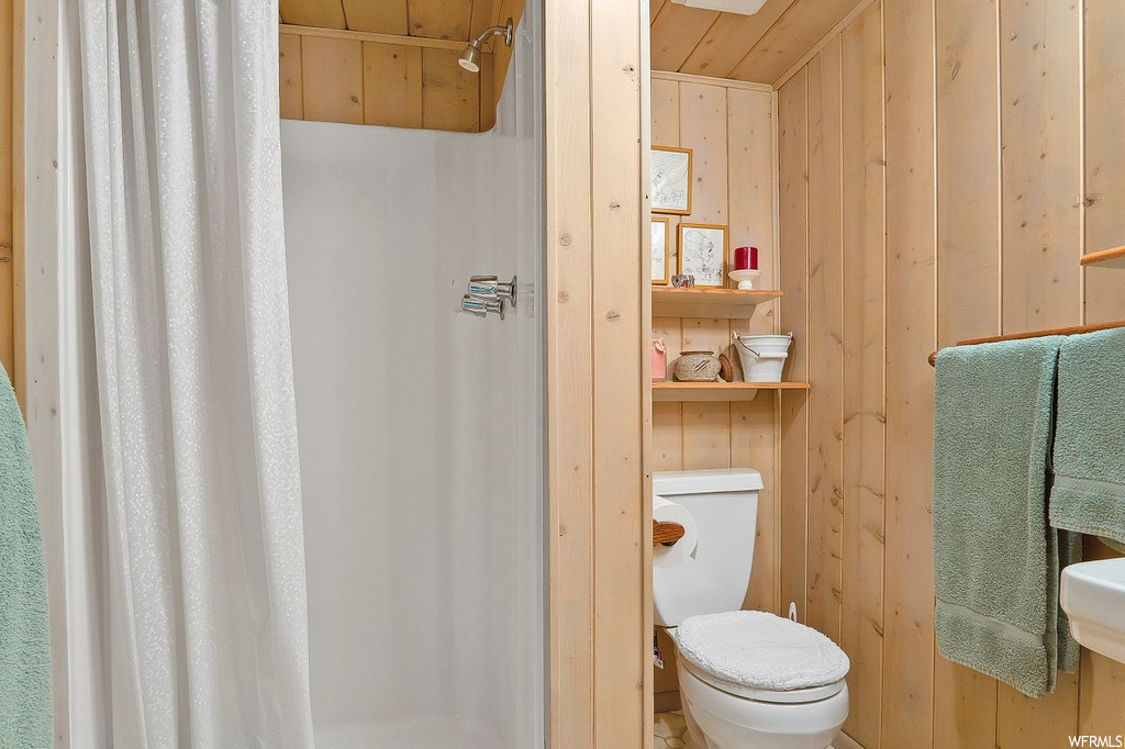 Bathroom featuring toilet, curtained shower, wood ceiling, and wood walls