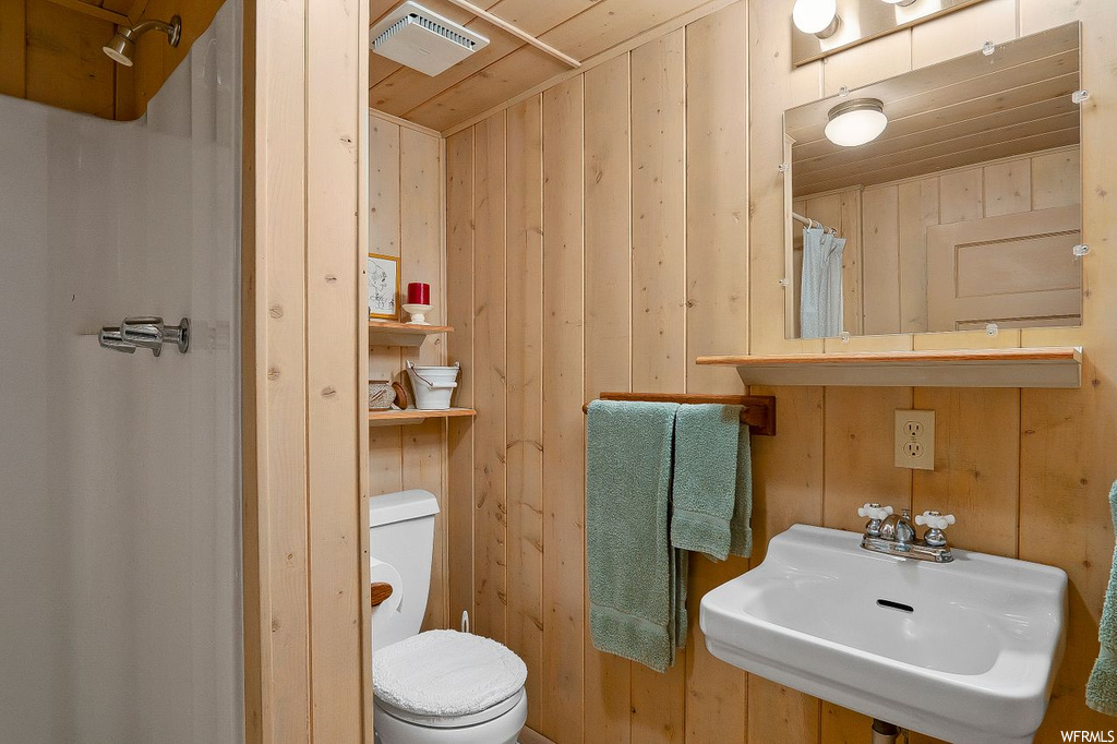 Bathroom with wooden walls, wooden ceiling, sink, and toilet
