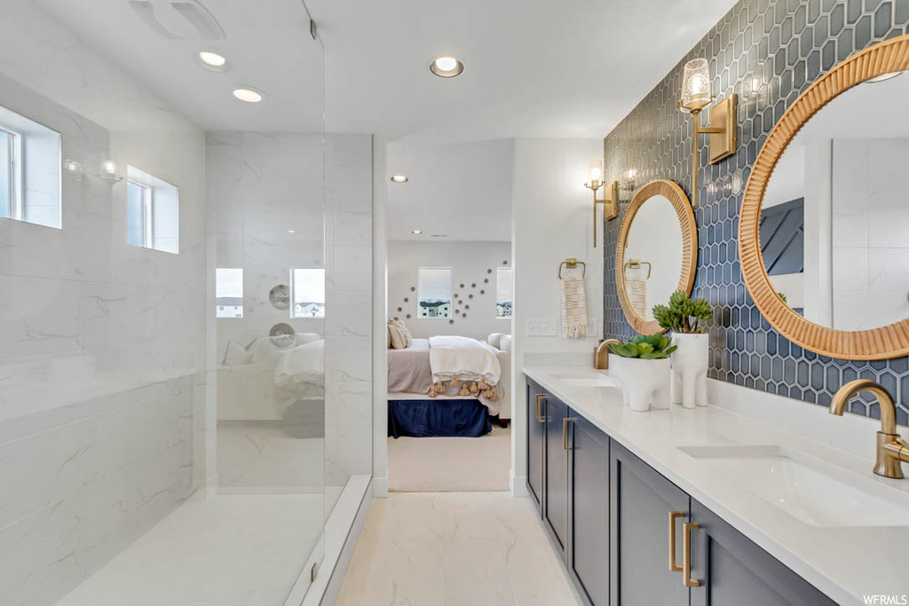 Bathroom featuring tile floors, tasteful backsplash, dual sinks, a tile shower, and vanity with extensive cabinet space