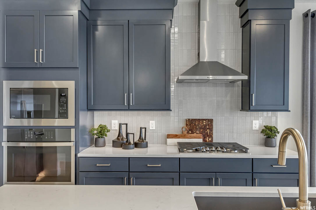 Kitchen featuring wall chimney range hood, stainless steel appliances, stone countertops light, backsplash, and sink