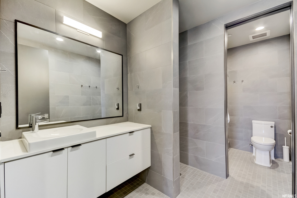 Bathroom with tile walls, large vanity, tile floors, and toilet