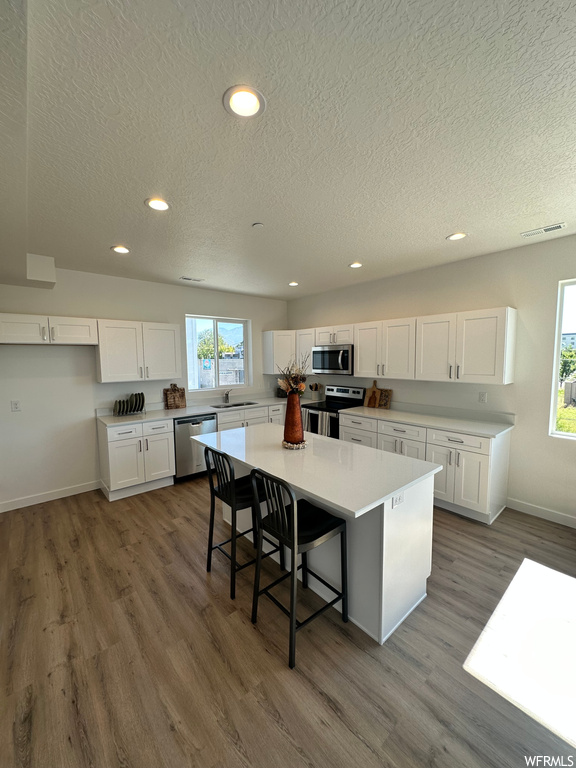 Kitchen featuring sink, white cabinets, hardwood flooring, a center island, and appliances with stainless steel finishes