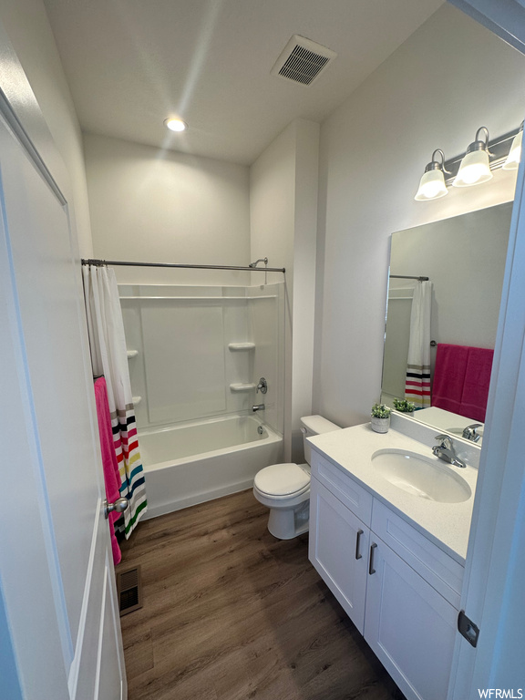Full bathroom featuring large vanity, toilet, hardwood floors, and shower / bathtub combination with curtain