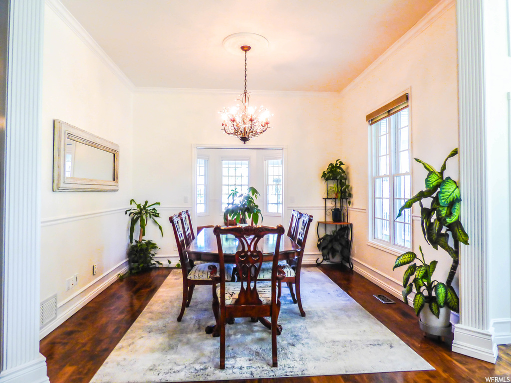 Wood floored dining area featuring plenty of natural light, an inviting chandelier, and ornamental molding