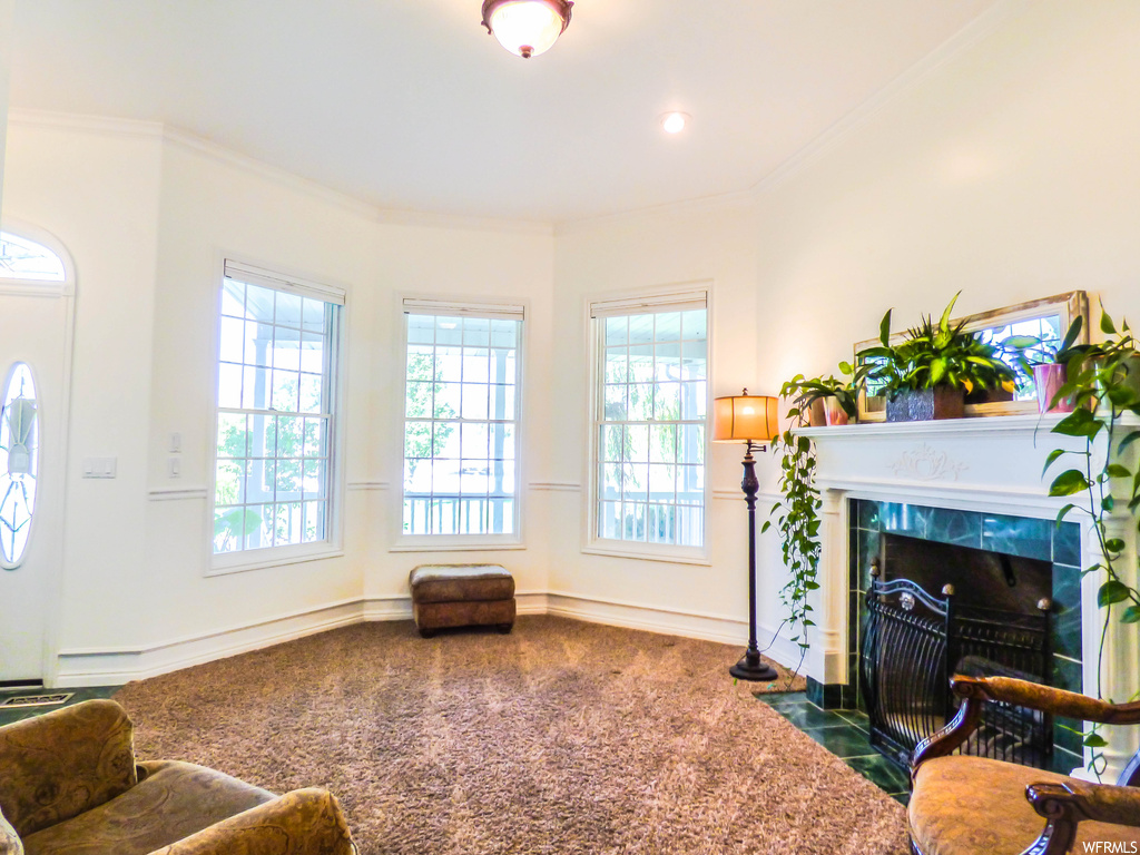 Carpeted living room with plenty of natural light, crown molding, and a tiled fireplace