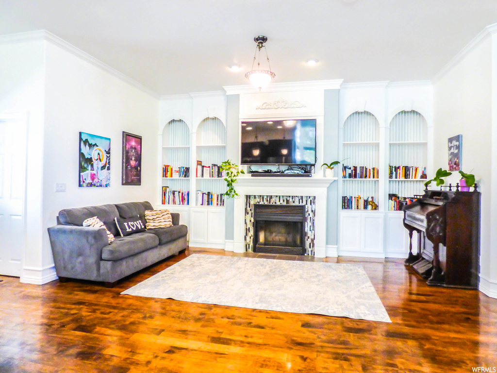 Hardwood floored living room with built in shelves, a tiled fireplace, and crown molding