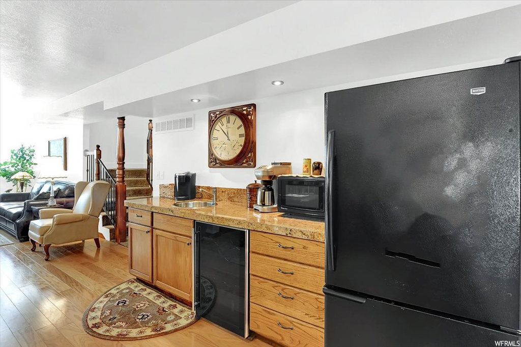 Kitchen with sink, wine cooler, black appliances, and light hardwood flooring