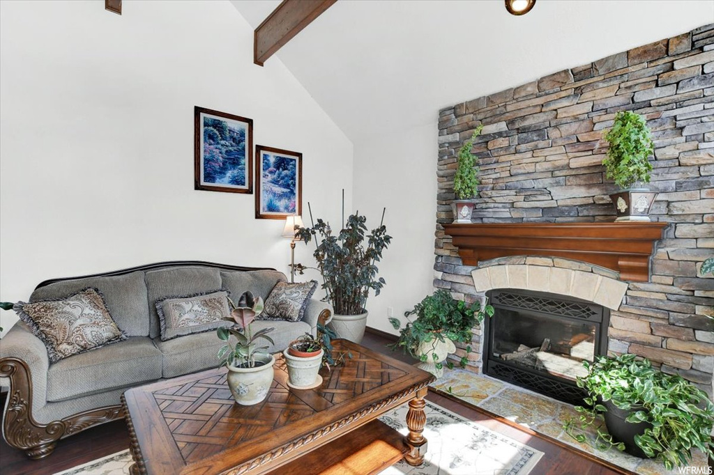 Hardwood floored living room featuring vaulted ceiling with beams and a fireplace