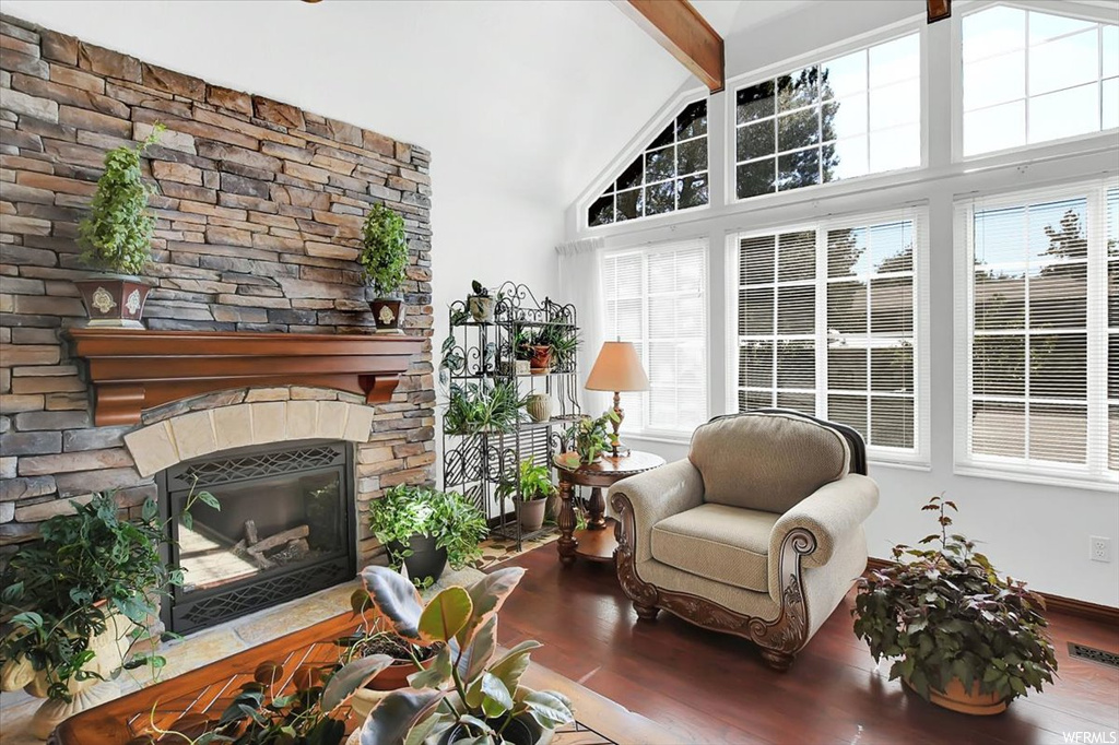 Hardwood floored living room featuring vaulted ceiling high, a stone fireplace, and beamed ceiling