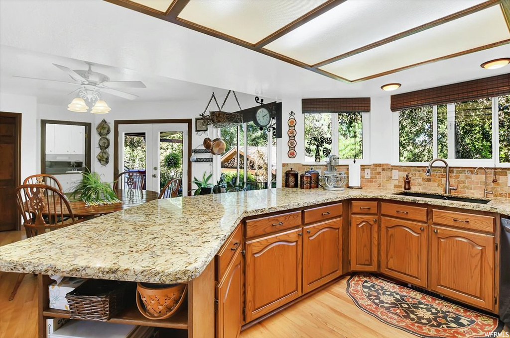 Kitchen with sink, ceiling fan, light hardwood flooring, tasteful backsplash, and light stone counters
