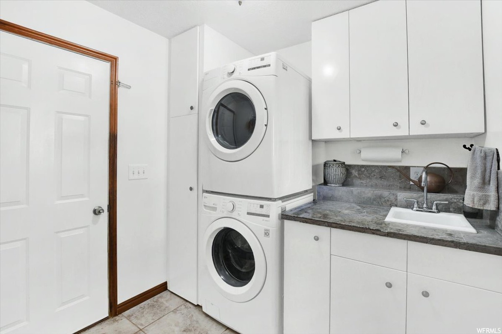 Laundry area with light tile floors, cabinets, sink, and stacked washing maching and dryer