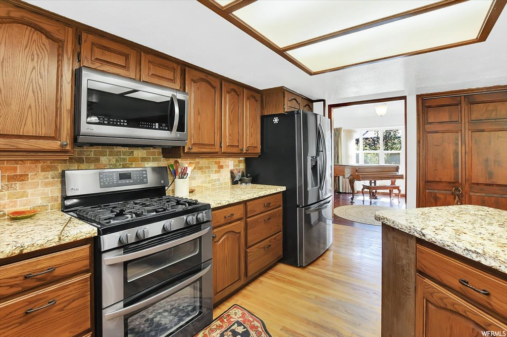 Kitchen featuring light stone countertops, backsplash, light hardwood floors, and appliances with stainless steel finishes