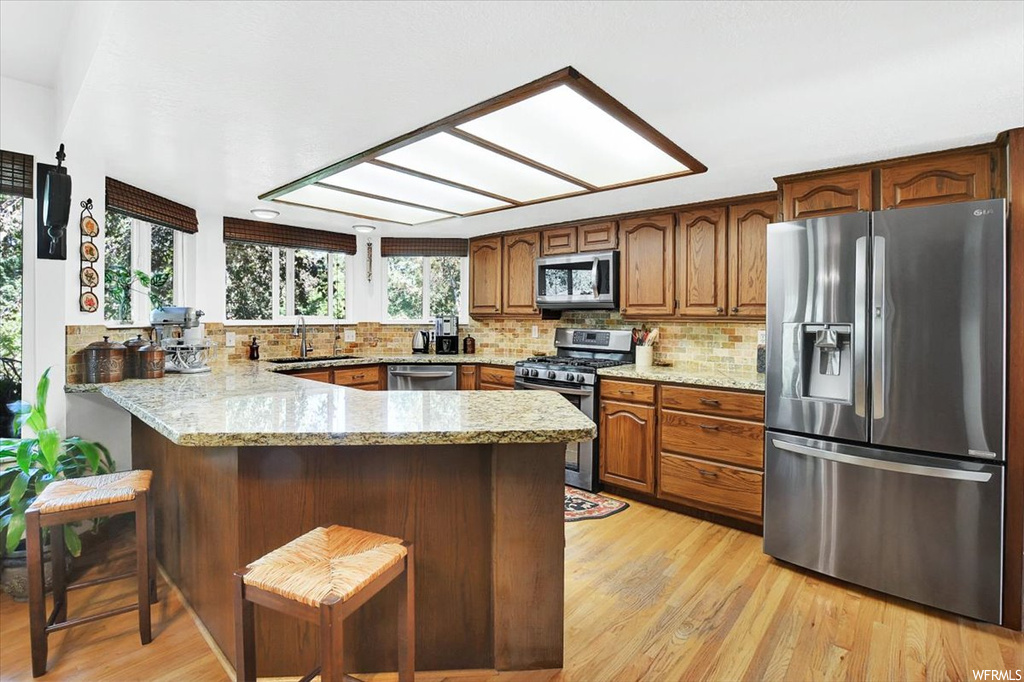 Kitchen featuring kitchen peninsula, tasteful backsplash, light stone counters, light hardwood flooring, and stainless steel appliances