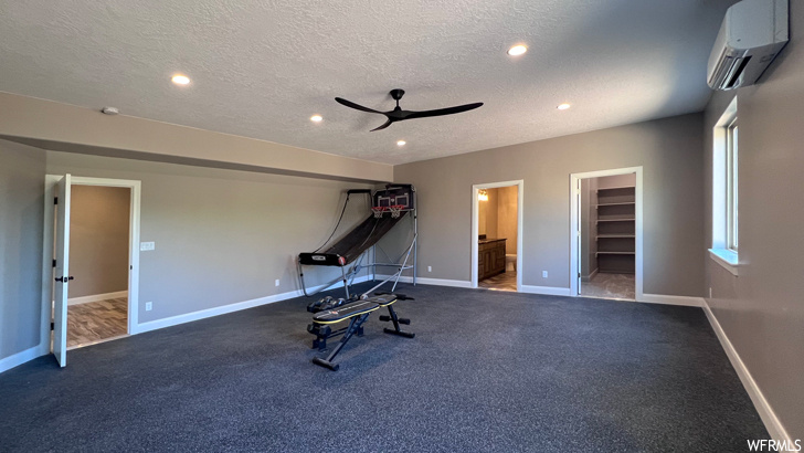 Workout room with ceiling fan, an AC wall unit, dark colored carpet, and a textured ceiling