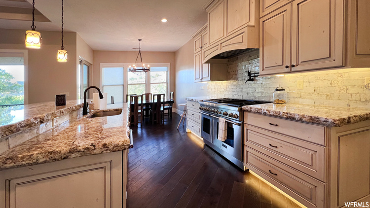 Kitchen with sink, range with two ovens, premium range hood, dark hardwood floors, and decorative light fixtures