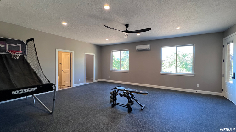 Exercise area with a textured ceiling, carpet flooring, a wall mounted AC, and ceiling fan