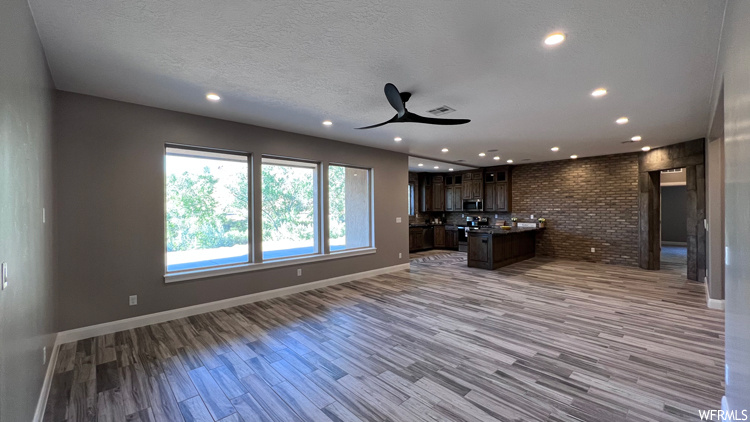 Kitchen featuring ceiling fan, a kitchen island with sink, light hardwood flooring, a textured ceiling, and dark brown cabinetry