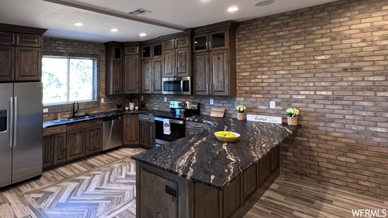 Kitchen featuring sink, brick wall, dark stone countertops, tasteful backsplash, and appliances with stainless steel finishes