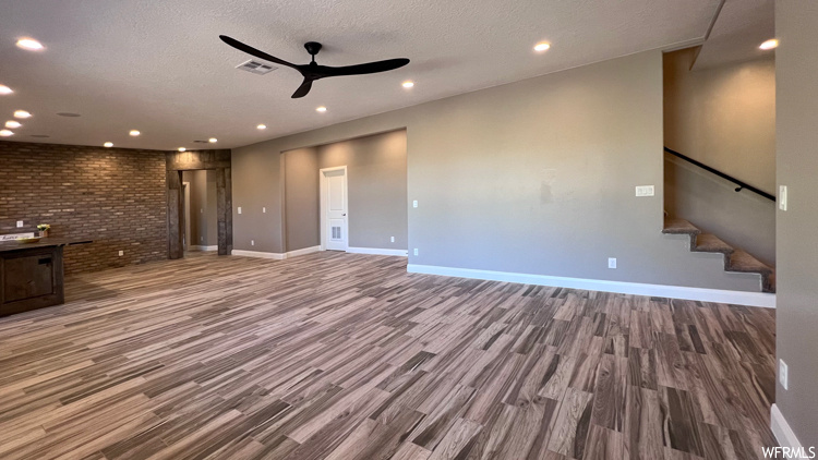 Unfurnished living room featuring dark hardwood flooring, ceiling fan, brick wall, and a textured ceiling