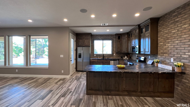 Kitchen with light hardwood flooring, dark stone countertops, tasteful backsplash, stainless steel appliances, and kitchen peninsula