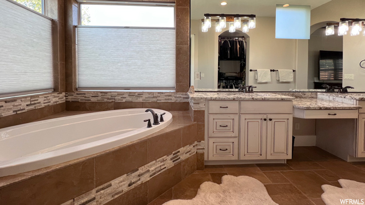 Bathroom featuring tiled tub, tile floors, and vanity with extensive cabinet space