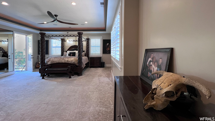 Bedroom with a tray ceiling, light carpet, access to exterior, and ceiling fan