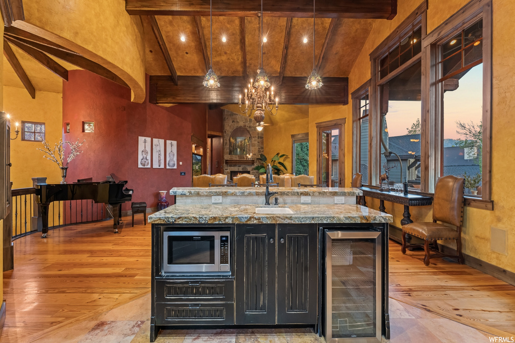 Kitchen with stainless steel microwave, wine cooler, hanging light fixtures, an inviting chandelier, and wood-type flooring