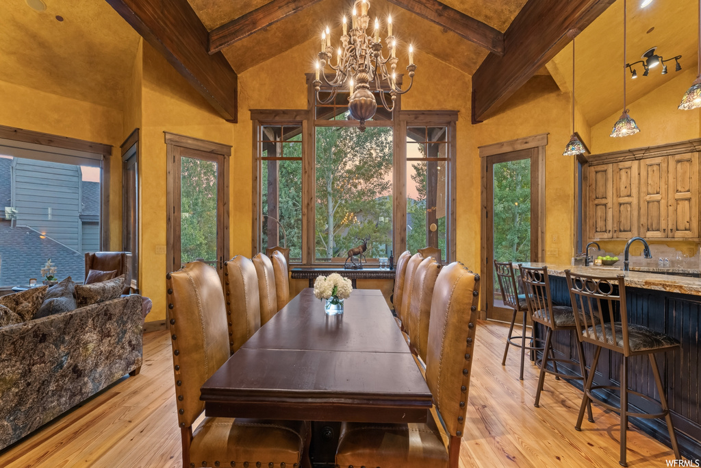 Dining space with vaulted ceiling high, light hardwood flooring, an inviting chandelier, and beamed ceiling