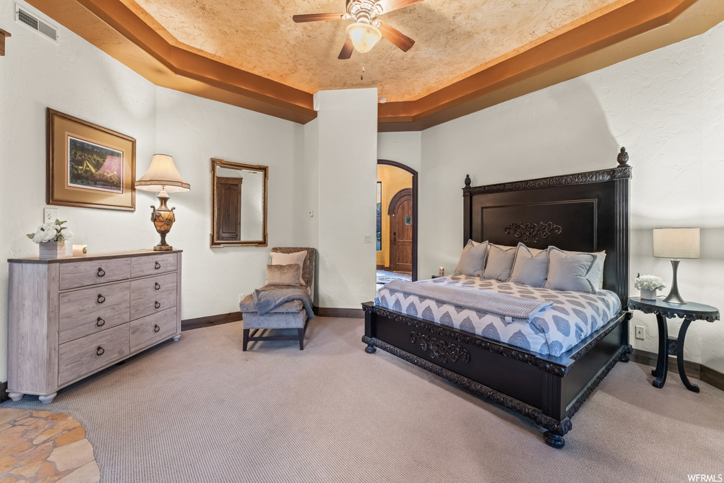 Bedroom featuring ceiling fan, a tray ceiling, and carpet flooring