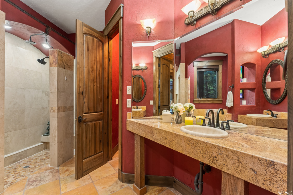 Bathroom with double sink, tile floors, large vanity, and tiled shower