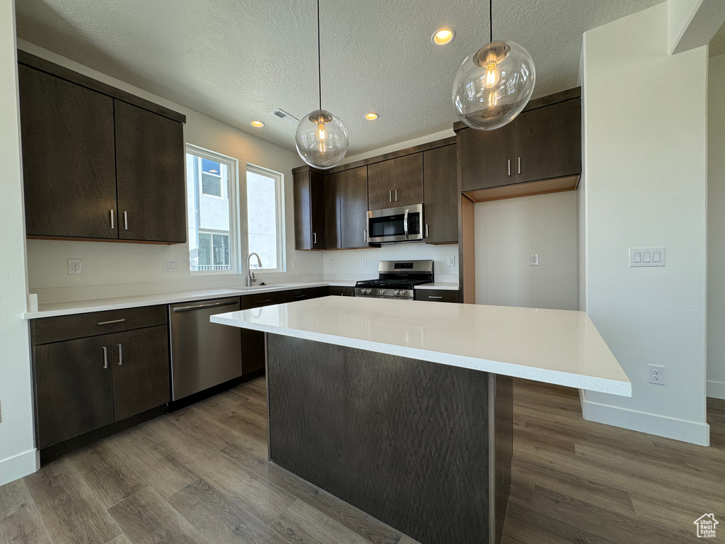 Kitchen featuring pendant lighting, stainless steel appliances, a kitchen island, and dark hardwood / wood-style flooring