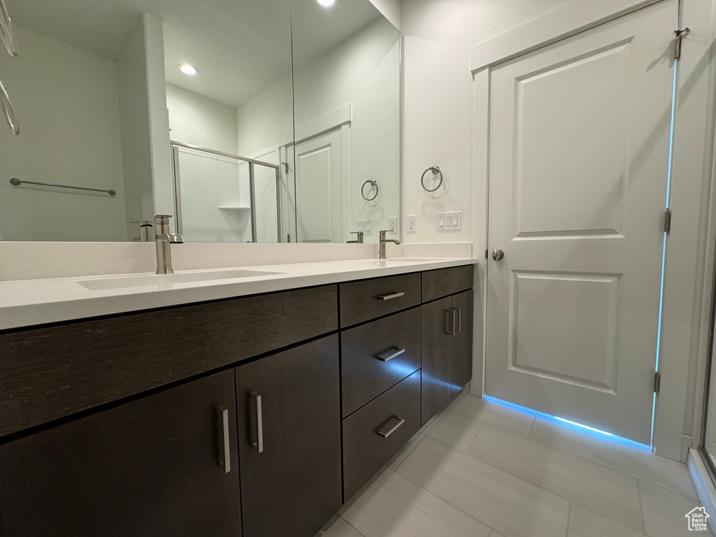 Bathroom featuring tile flooring, large vanity, walk in shower, and dual sinks