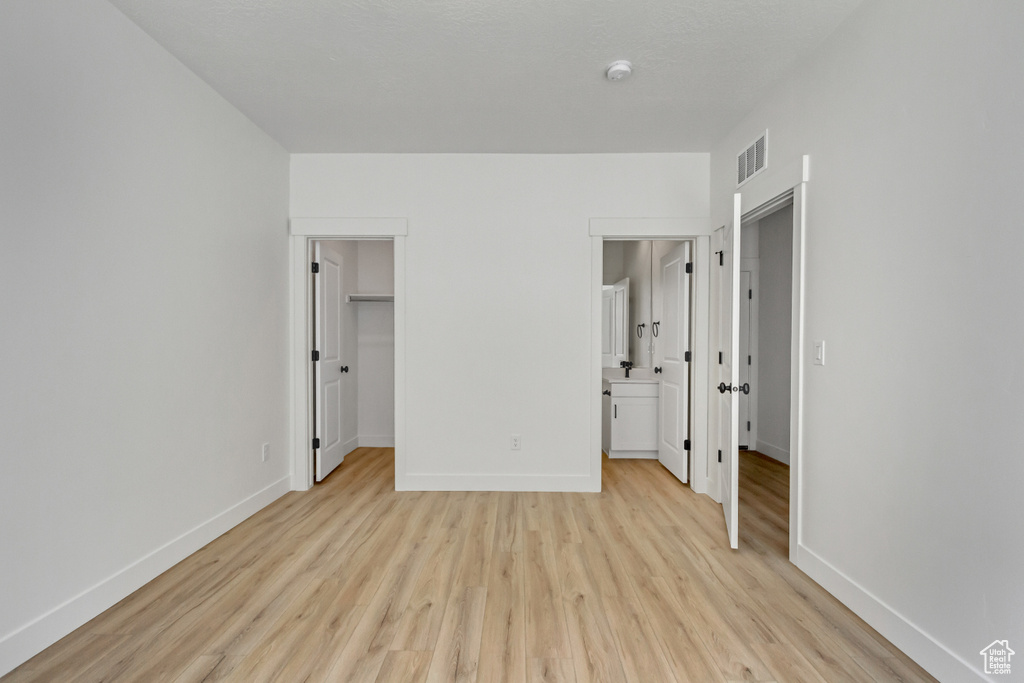 Unfurnished bedroom featuring connected bathroom, a closet, light hardwood / wood-style floors, and a spacious closet
