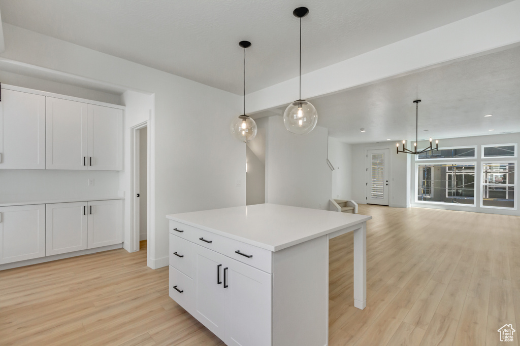 Kitchen with pendant lighting, white cabinetry, a notable chandelier, a kitchen island, and light hardwood / wood-style floors