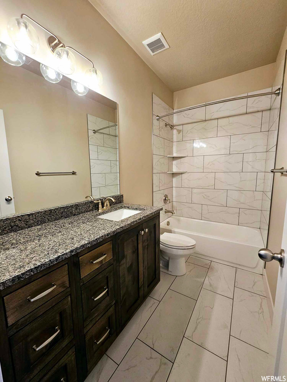 Full bathroom with toilet, vanity, a textured ceiling, tiled shower / bath, and tile floors