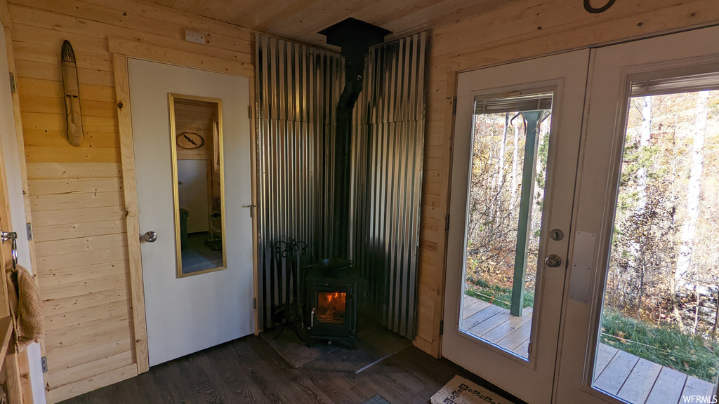 Doorway with french doors, wooden walls, dark hardwood flooring, and a wood stove