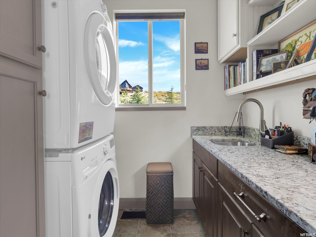 Laundry room with sink, cabinets, stacked washer / dryer, and dark tile flooring