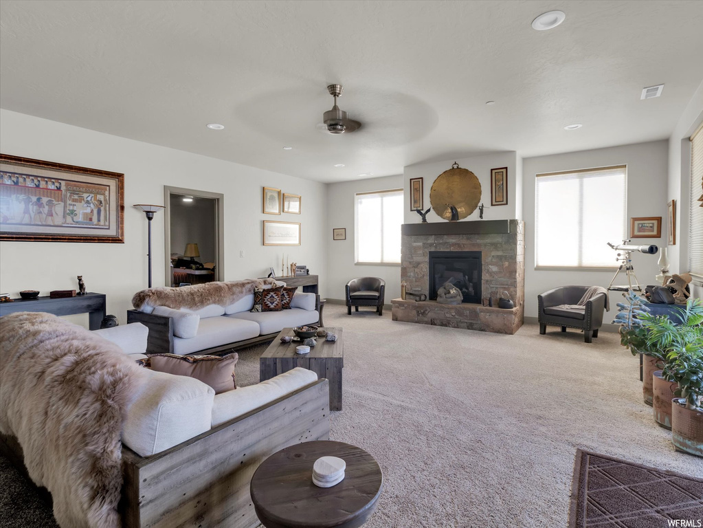 Carpeted living room featuring ceiling fan and a stone fireplace