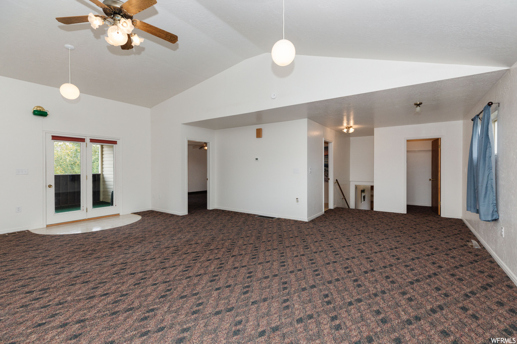 Empty room featuring ceiling fan, dark carpet, and lofted ceiling