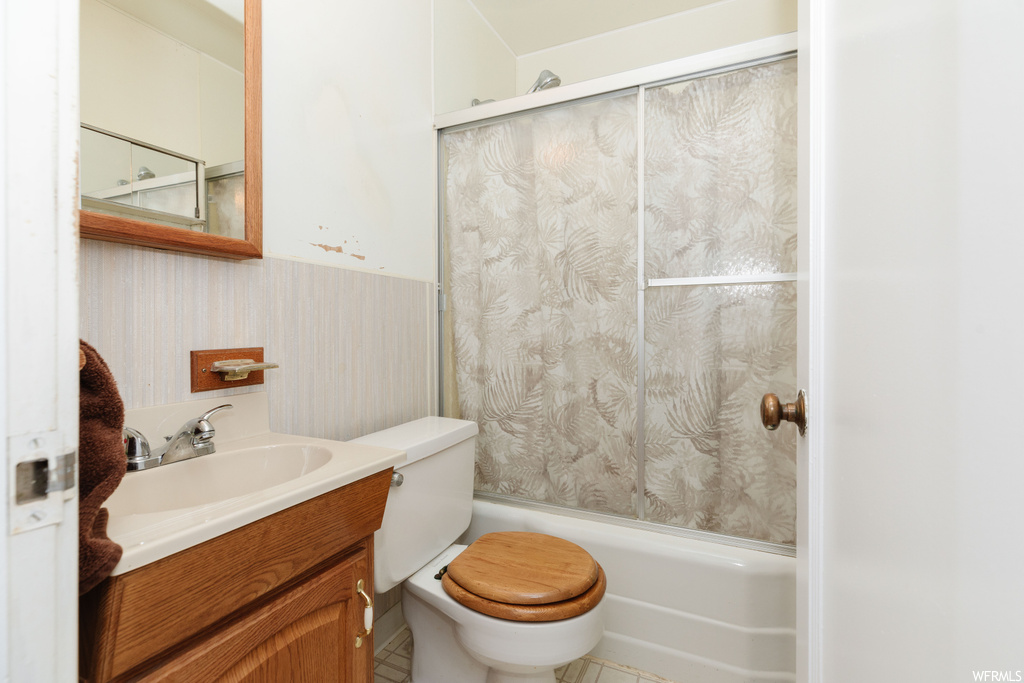Full bathroom with combined bath / shower with glass door, vanity, tile flooring, and toilet